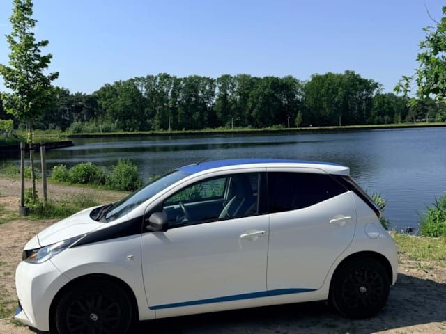 Witte Toyota Aygo (2015) met blauw dak en blauwe sierstreep, geparkeerd aan het water